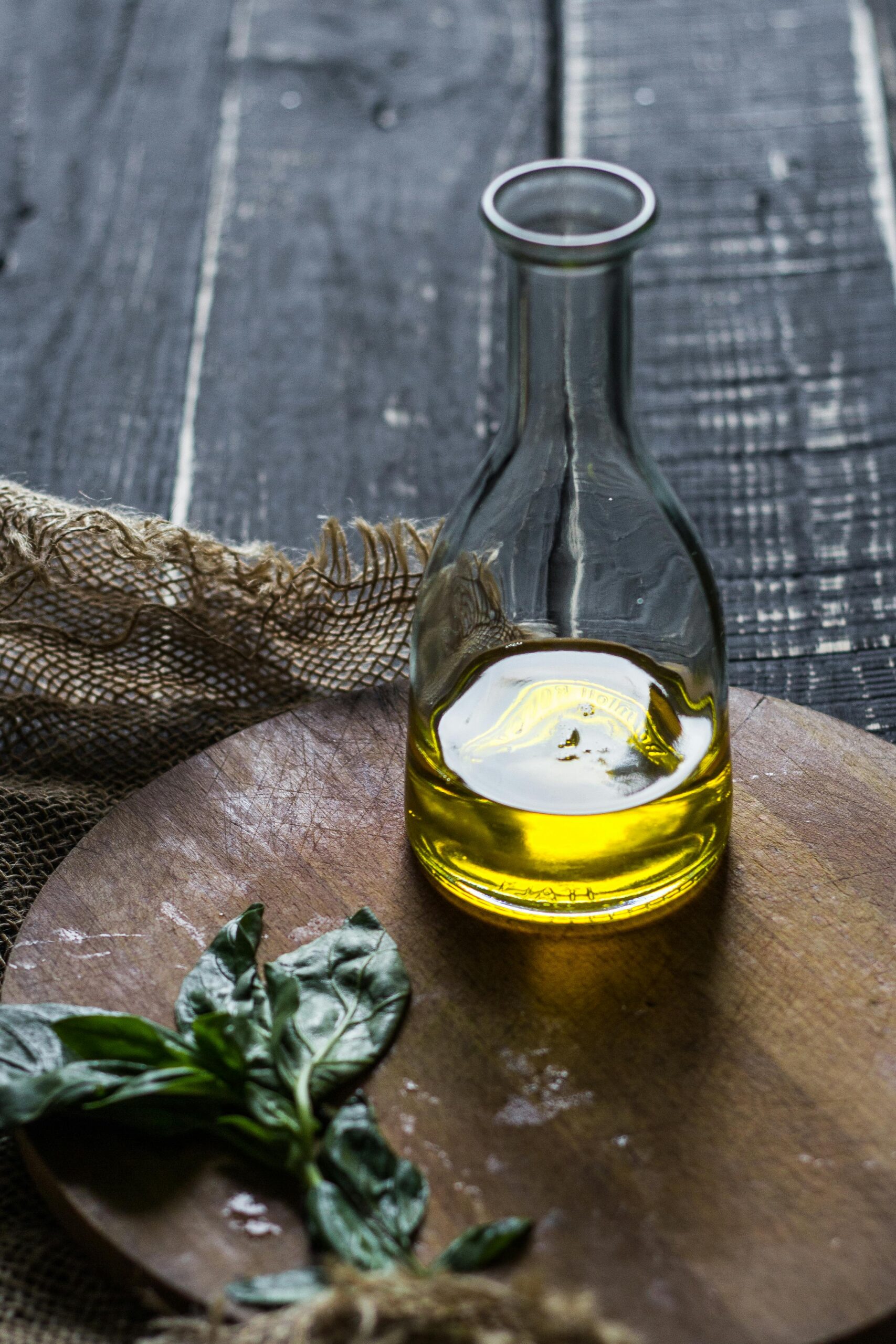 A bottle of olive oil with fresh basil leaves on a wooden cutting board, perfect for cooking inspiration.
